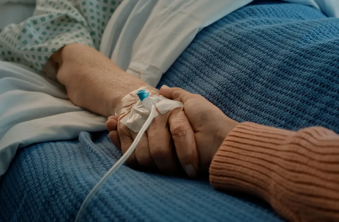 Patient in a hospital bed holding a relative’s hand